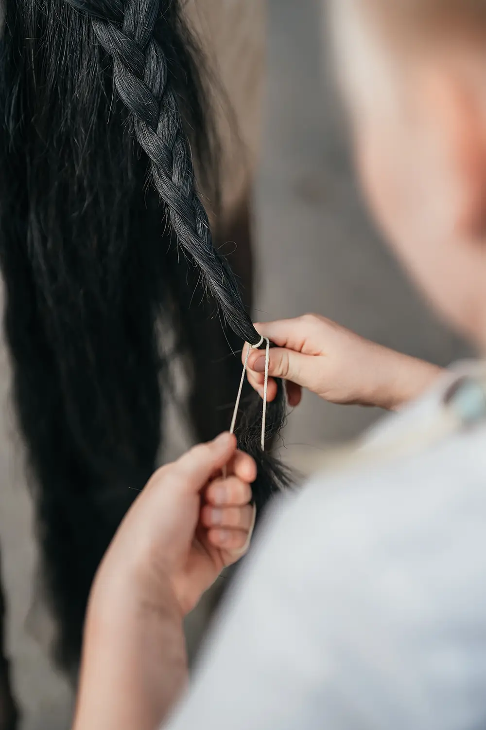 Detailaufnahme: Die Hände eines Mädchen flechten die Mähne eines schwarzen Ponys auf Hof Mormann