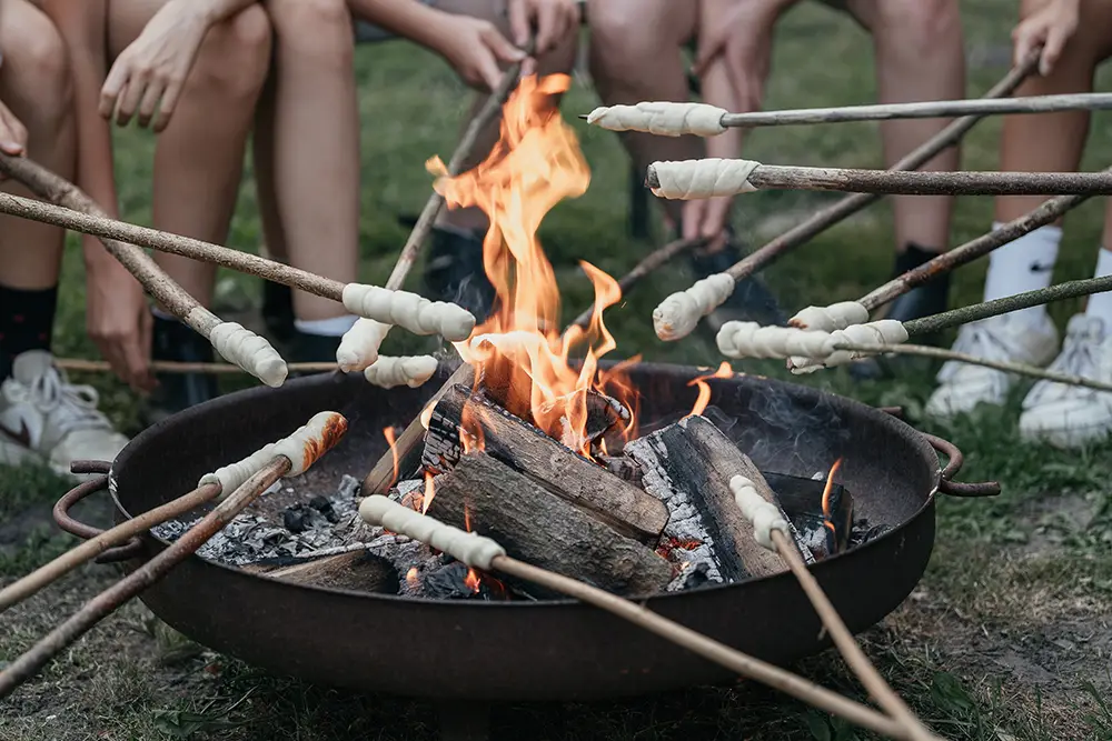 Klassenfahrt Viele Stockbrote werden bei einer Klassenfahrt über eine Feuerschale gehalten.
