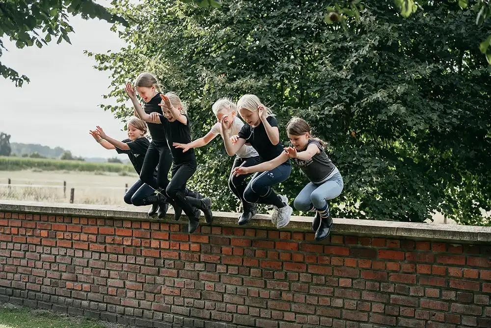 Klassenfahrt Die Mädchen spielen und springen auf der Mauer am Hofesrand