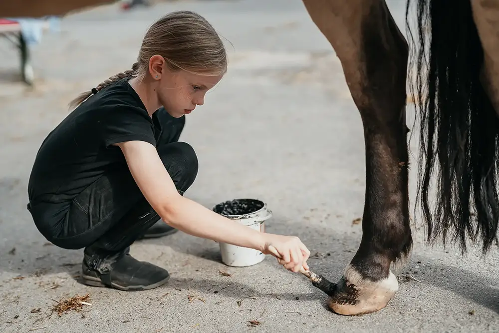 Ein Mädchen trägt Hufschutz auf eine Pferdehufe auf