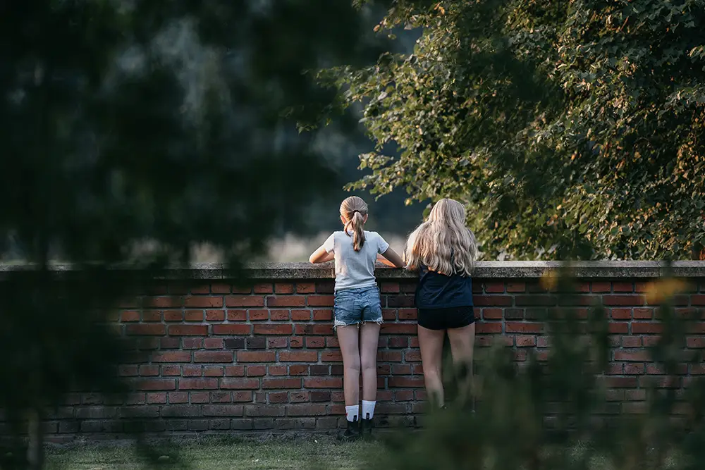 Zwei Mädchen stehen an der Mauer am Feldrand und schauen in die Ferne