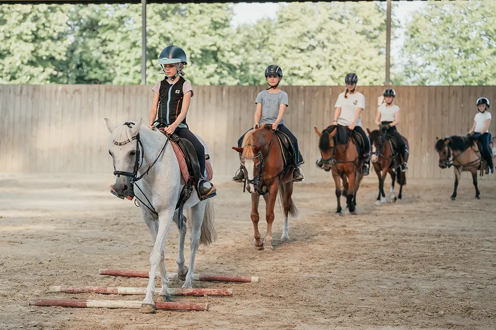 Mehrere Mädchen reiten in einer Linie hintereinander her beim Reitunterricht in der Reithalle auf Hof Mormann in Havixbeck